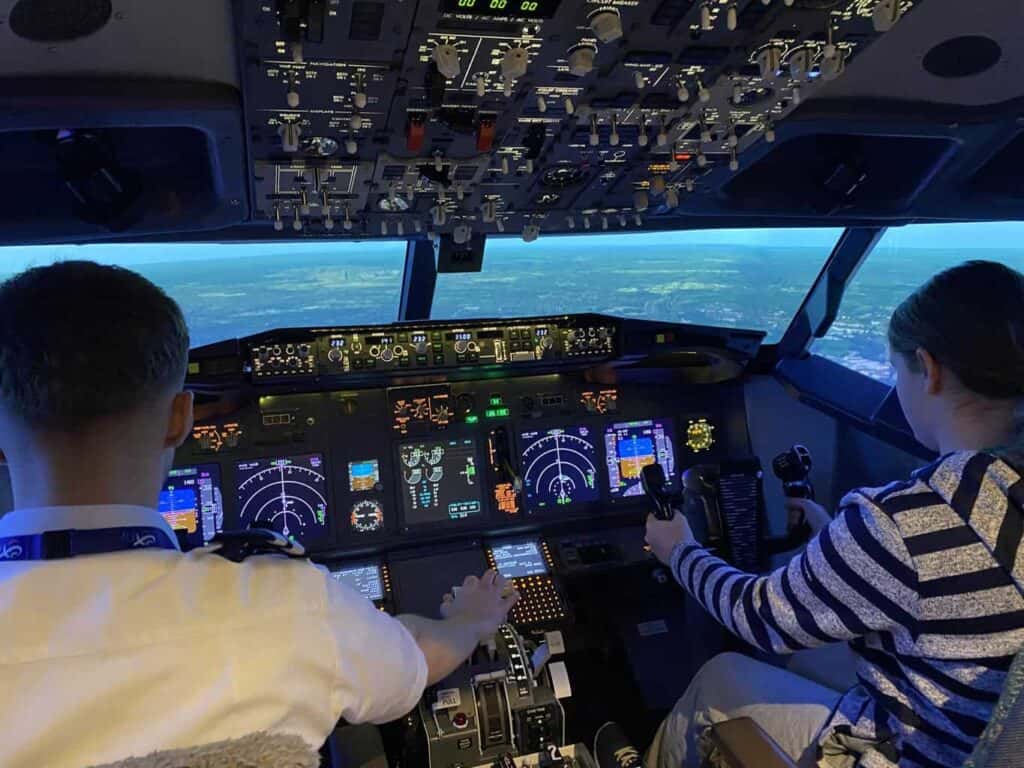 Peggy is sat in the pilot chair of a flight simulator ready to the land the plane with the help of a pilot as part of the aviation career day 
