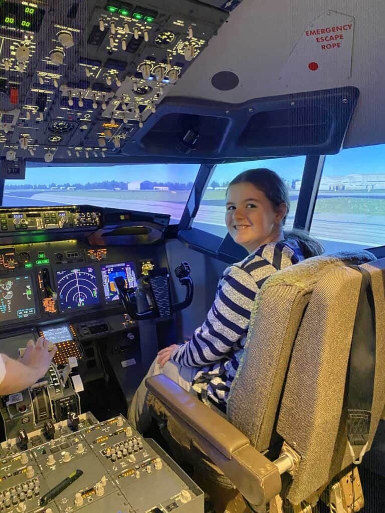 Peggy is sat in the pilot chair of a flight simulator ready to the land the plane as part of the aviation career day 