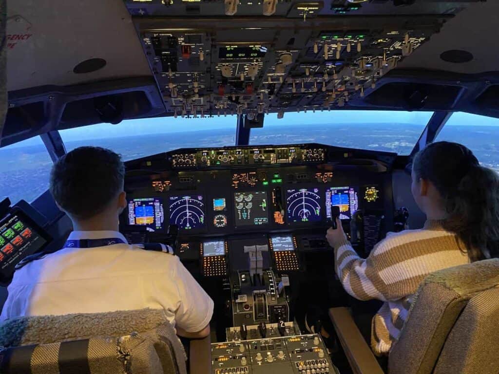Peggy is sat in the pilot chair of a flight simulator ready to the land the plane with the help of a pilot as part of the aviation career day 