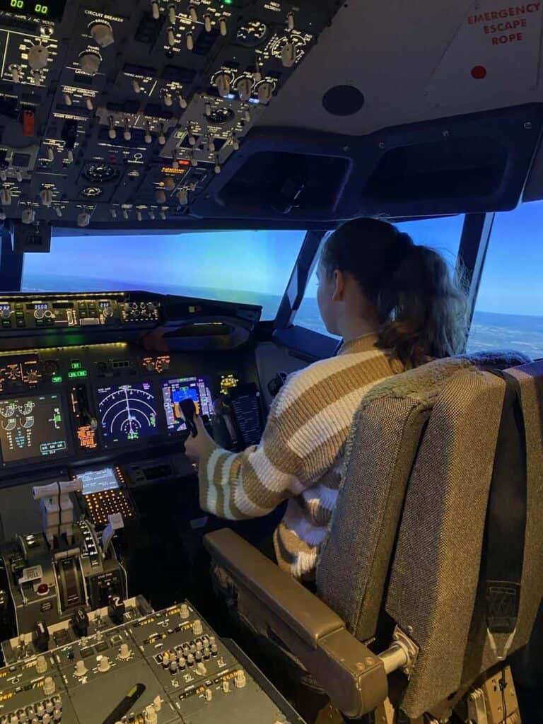 Aggie is sat in the pilot chair of a flight simulator ready to the land the plane with the help of a pilot as part of the aviation career day 