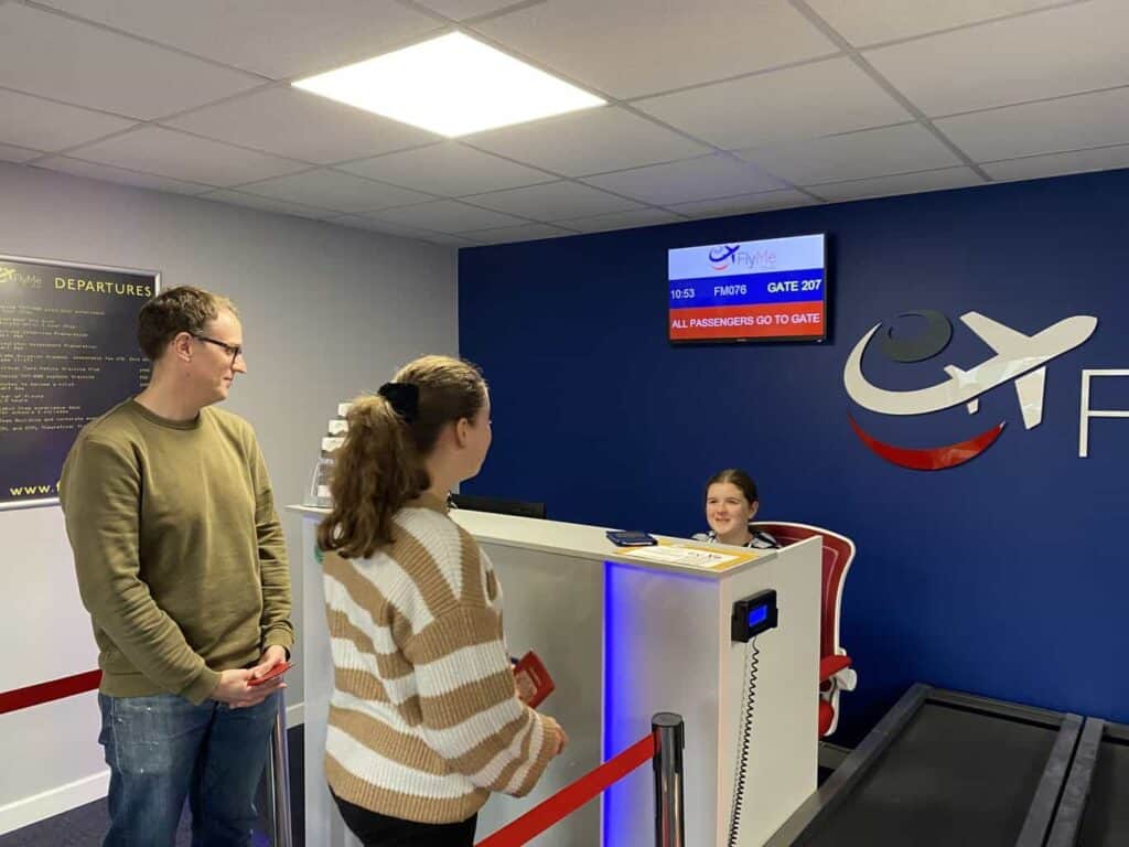 Peggy is sitting at a check-in desk checking Aggie onto her flight as part of the aviation career day 